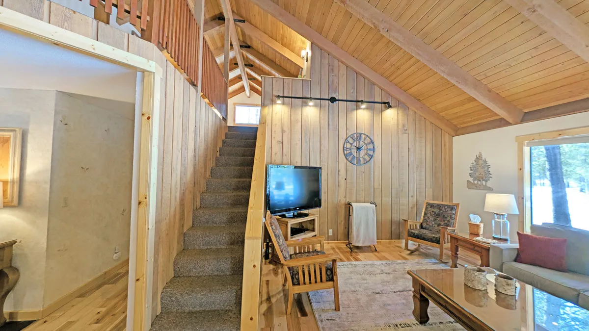A warm, welcoming area with a staircase, wooden walls, a TV, and a comfortable seating area. The space is suitable for socializing, watching movies, or simply relaxing, and connects the upstairs hangout zones with the main living area below.