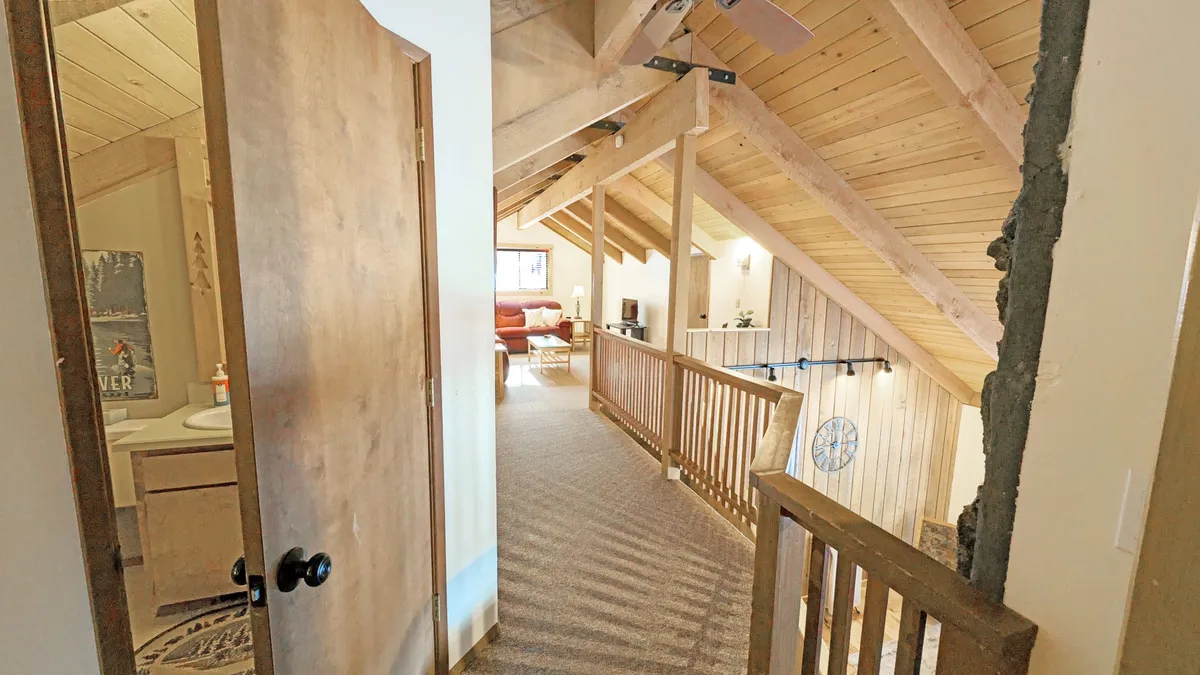 A cozy open loft area with visible wooden beams, a decorative wall clock, and comfortable seating. The space feels inviting and is ideal for relaxing, reading, or spending time with family. Natural light streams in, enhancing the sense of openness and comfort.