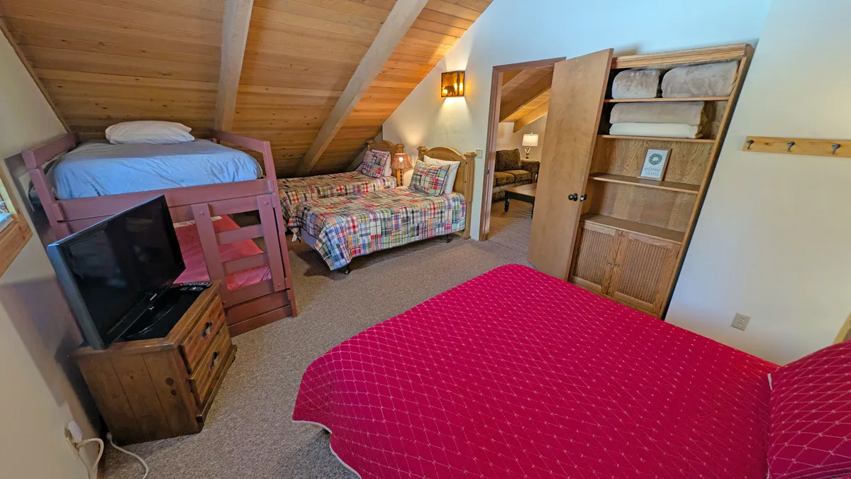 A family-friendly bedroom featuring a bunk bed, double bed with plaid bedding, wooden accents, and a television. The space is designed for group sleepovers and family gatherings, providing both comfort and a social atmosphere.