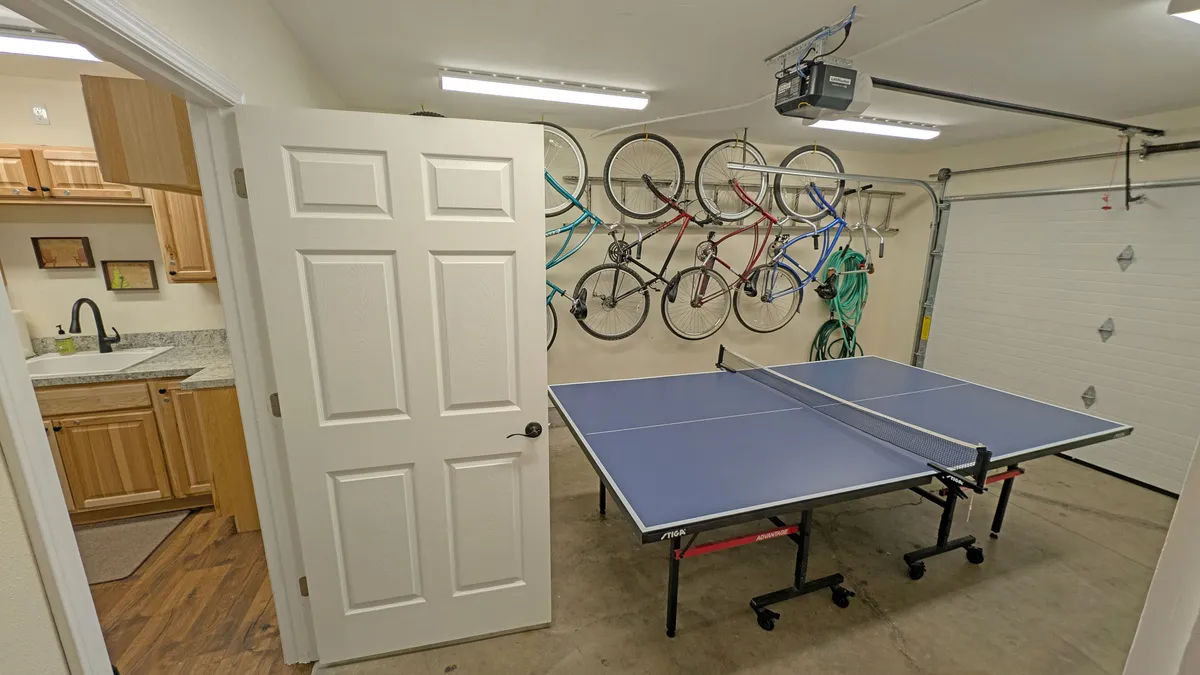 This image showcases a ping pong table, bicycles mounted on the wall, and a kitchen area in the background. The visible bikes immediately connect to the adventure and exploration theme, while the open, active mood hints at preparing for outings or returning from trail rides.