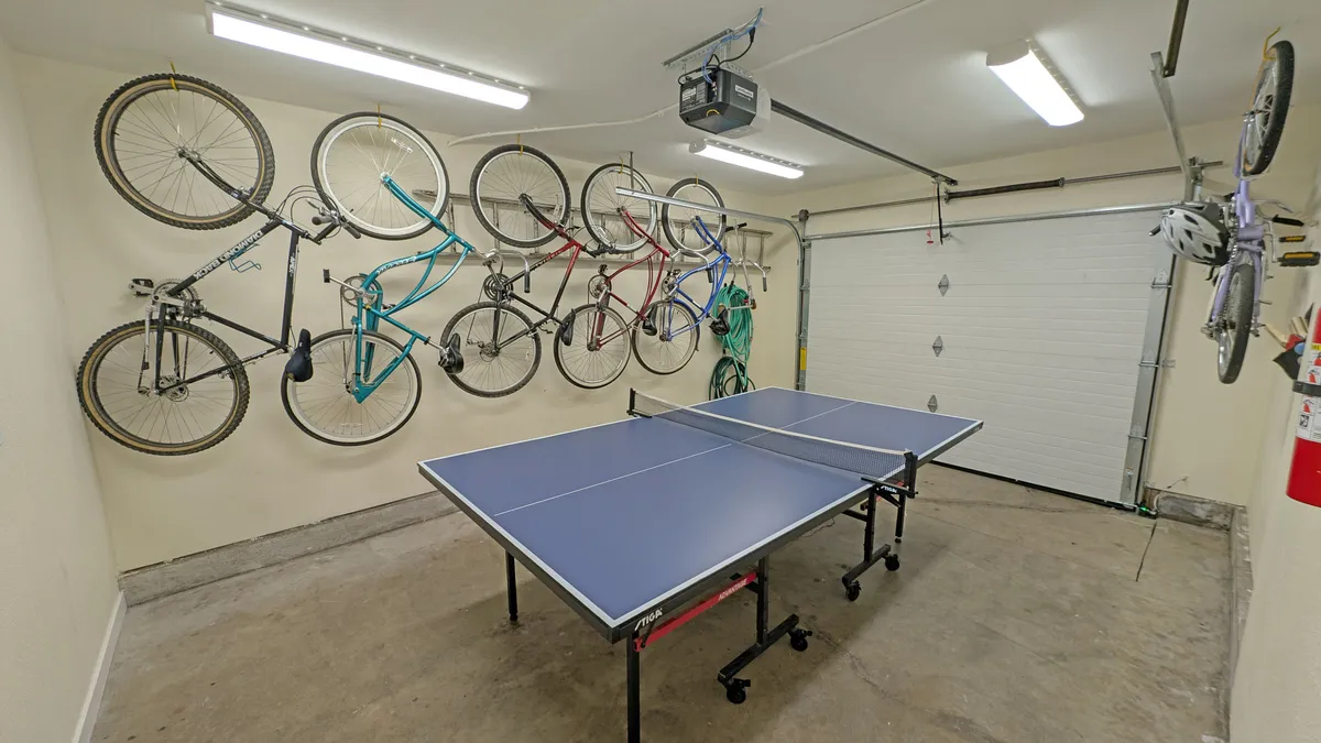 Inside the home, this scene highlights a spacious area with a ping pong table and several bicycles mounted on the wall. The space is energetic and hints at adventure, with the bikes ready for use and the ping pong table offering another option for active indoor fun.
