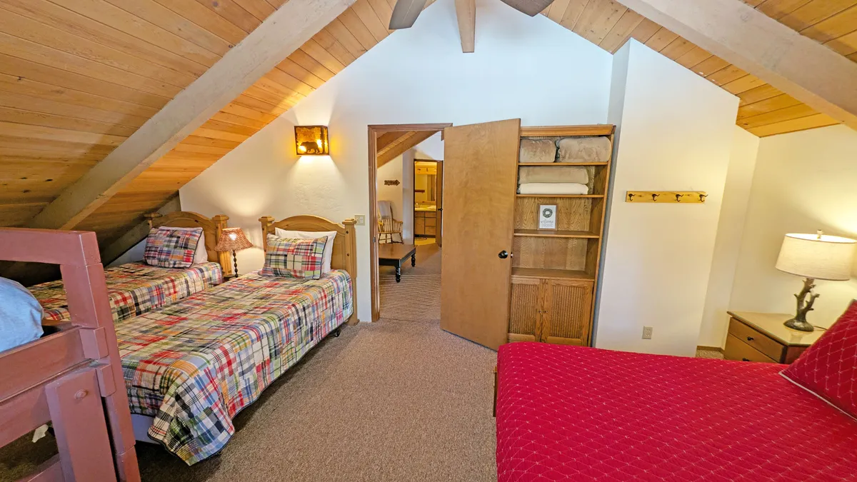 A charming kids’ or teens’ bedroom with plaid bunk beds, a red accent chair, and wooden shelves, all bathed in inviting light. The playful, spacious ambiance encourages family stories and relaxation after outdoor adventures.