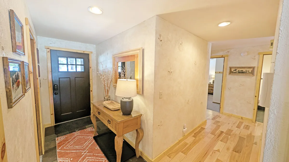 This image features a welcoming interior view of the front door area, adorned with a console table, lamp, rug, and attractive artwork. The space exudes warmth and personal touches, inviting guests to feel at home the moment they step inside.