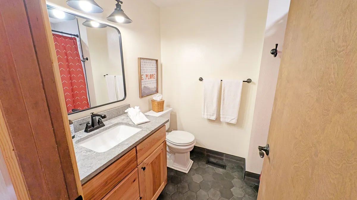 A modern bathroom with a large mirror, black faucet, red shower curtain, and towels neatly arranged. The space feels inviting and functional, designed for refreshing routines after a day of adventure.