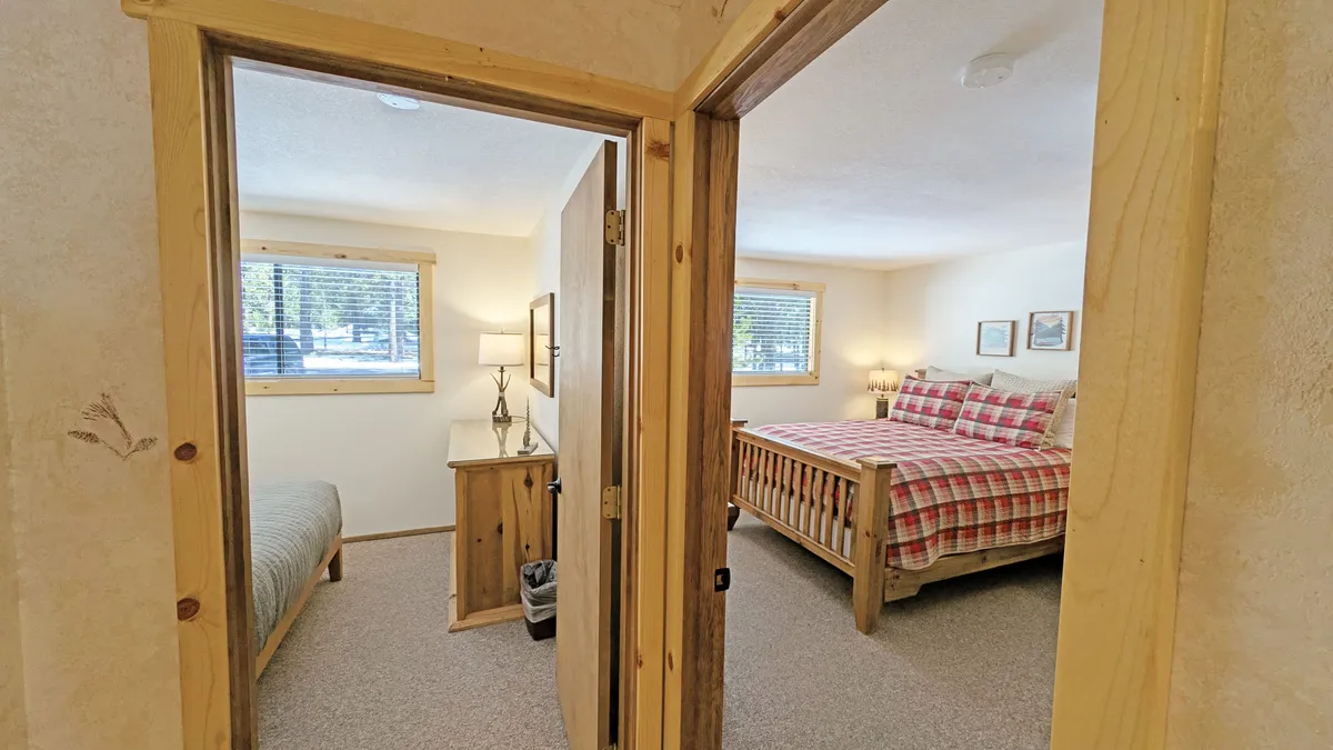 A view of two distinct bedrooms with wooden furniture and plaid bedding, sunlight streaming through the windows, and an overall atmosphere of comfort and privacy—ideal for families or couples seeking quiet retreats.
